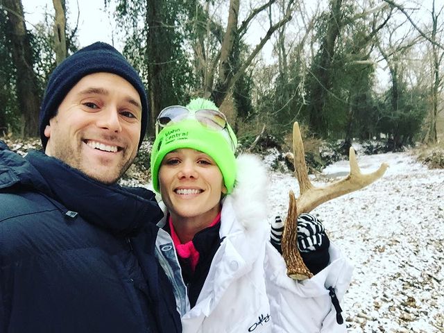 Graham is wearing a black jacket and cap, where as his girlfriend is wearing a white jacket with white-black gloves and green cap